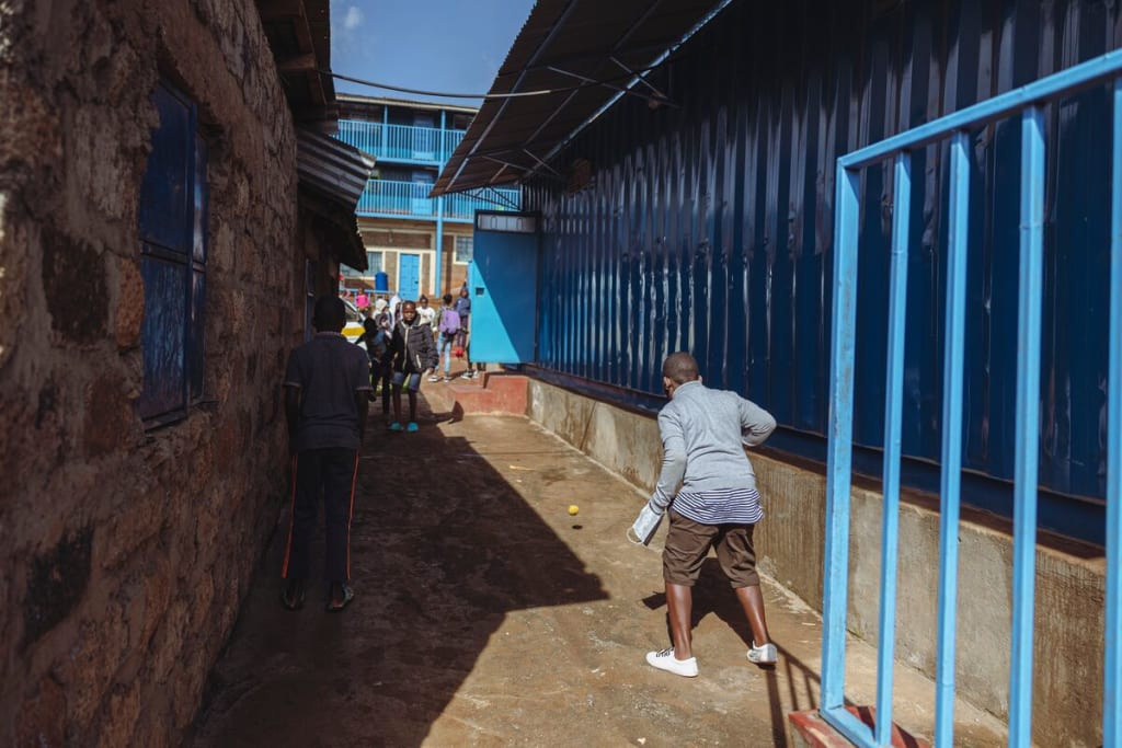 A boy runs along the side of a blue building